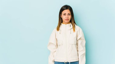 Mavi arka planda izole edilmiş genç bir kadın yanakları patlatır, yorgun bir ifade takınır. Yüz ifadesi kavramı.