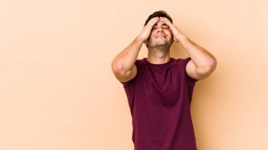 Bej arka planda izole olmuş genç bir adam ellerini başının üstünde tutarak neşeyle gülüyor. Mutluluk kavramı.