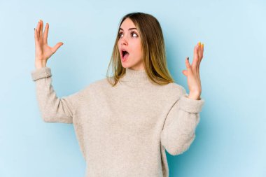 Mavi arka planda izole edilmiş genç beyaz kadın gökyüzüne haykırıyor, yukarı bakıyor, hayal kırıklığına uğramış..