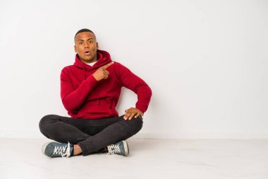 Yerde tek başına oturan genç latin adam yan tarafı gösteriyor.