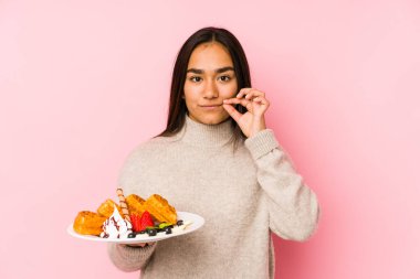 Genç Asyalı bir kadın waffle tutuyor. Parmakları dudaklarında ve bir sırrı saklıyor..