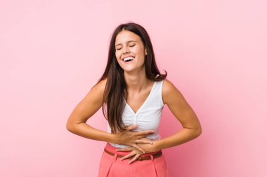 Genç ve güzel bir kadın mutlu bir şekilde gülüyor ve ellerini karnının üstünde tutarak eğleniyor..
