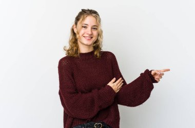 Beyaz arka planda genç beyaz kadın işaret parmağıyla işaret ederek gülümsüyor..