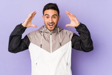 Mor arka planda izole olmuş genç beyaz bir adam zaferi ya da başarıyı kutluyor, şaşırıyor ve şok oluyor..