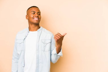 Genç latin adam bej arka planda izole edilmiş, başparmak uzakta, gülüyor ve kaygısız..