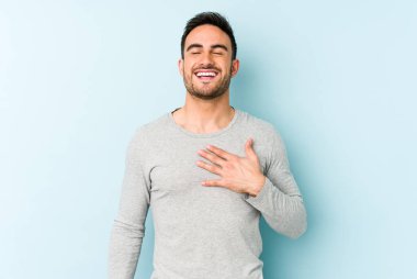 Young caucasian man isolated on blue background laughs out loudly keeping hand on chest. clipart