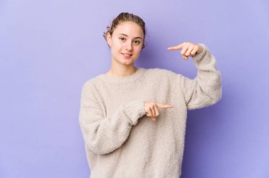 Mor arka planda genç beyaz bir kadın işaret parmaklarıyla küçük bir şey tutuyor, gülümsüyor ve kendinden emin..