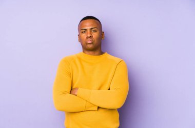 Mor arka planda izole edilmiş genç latin adam yanakları patlatıyor, yorgun bir ifadesi var. Yüz ifadesi kavramı.