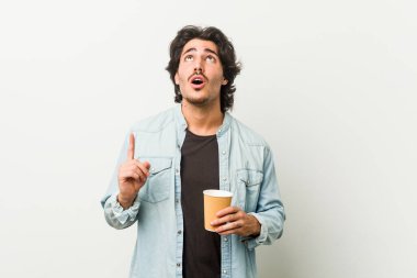 Genç, havalı bir adam kahvesini yukarıyı göstererek içiyor..