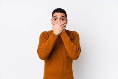 Beyaz arka planı olan genç bir latin adam elleri ile ağzını kapatırken şok oldu..