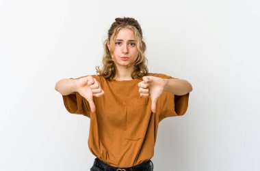 Beyaz arka planda genç beyaz bir kadın baş parmağını aşağı gösteriyor ve hoşlanmadığını ifade ediyor..