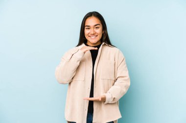 Mavi arka planda izole edilmiş genç bir kadın iki eliyle bir şey tutuyor, ürün sunumu..