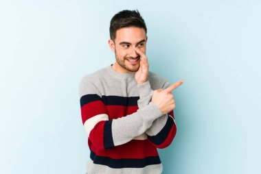 Kafkasyalı genç adam mavi arka planda izole edilmiş. Dedikodu yapıyor, bir şeyleri bildiriyor..