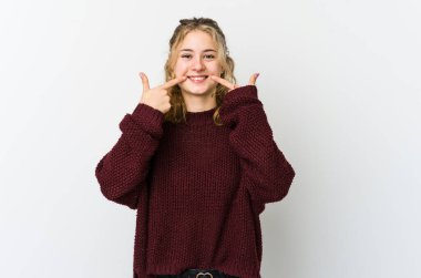 Beyaz arka planda genç beyaz kadın gülümsüyor, parmaklarını ağıza doğrultuyor..