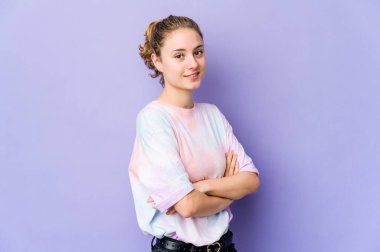 Mor arka planda kendini güvende hisseden, kararlılıkla kollarını kavuşturan beyaz bir kadın..