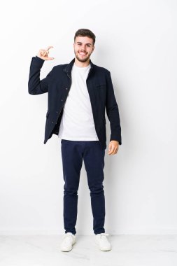 Tam vücut Kafkasyalı genç bir adam, izole edilmiş, işaret parmaklarıyla küçük bir şey tutuyor, gülümsüyor ve kendinden emin..