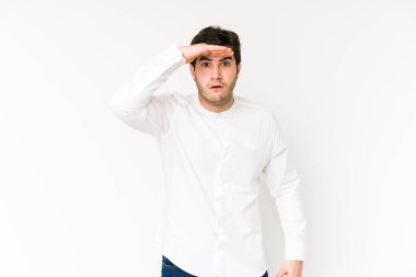 Genç adam beyaz arka planda izole edilmiş. Uzağa bakıyor. Elini alnına koyuyor..