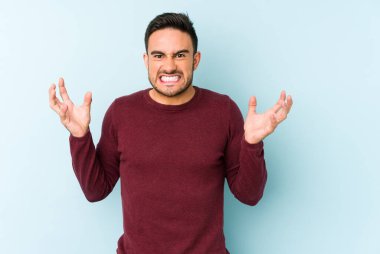 Mavi arka planda izole edilmiş genç beyaz adam öfkeyle bağırıyor..