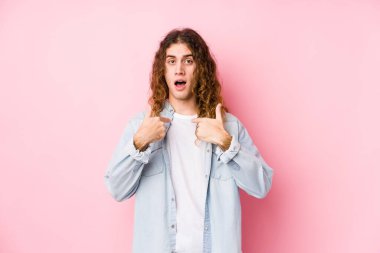 Uzun saçlı adam yalnız poz veriyor. Parmakla işaret ediyor, gülümsüyor..