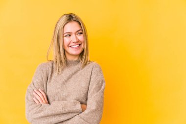 Sarı arka planda soyutlanmış genç sarışın kadın kollarını kavuşturarak gülümsüyor..