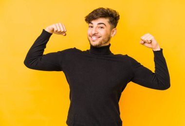 Sarı arka planda izole edilmiş genç bir Arap erkek güçlü bir hareket gösteriyor, kollarıyla, kadınsı gücün sembolü.