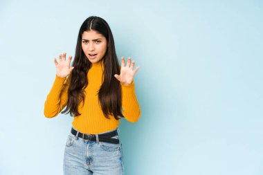 Mavi arka planda izole edilmiş genç Hintli kadın pençelerini kedi taklidi yaparken gösteriyor, agresif bir hareket..