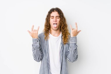 Genç, uzun saçlı, izole bir şekilde poz veren adam parmaklarıyla kaya hareketi yapıyor.