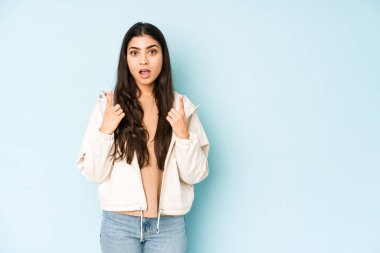 Mavi arka planda genç Hintli kadın ağzı açık bir şekilde üst tarafı işaret ediyor..