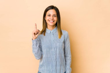Bej arka planda izole edilmiş genç bir kadın bir numarayı parmağıyla gösteriyor..