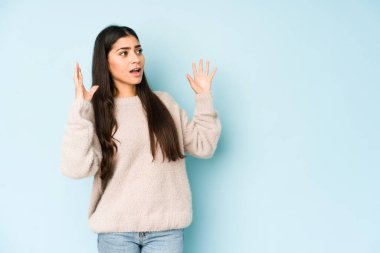 Genç Hintli kadın mavi arka planda izole edilmiş, gökyüzüne haykırıyor, yukarı bakıyor, hayal kırıklığına uğramış..