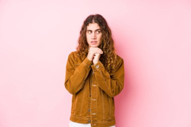 Uzun saçlı yalnız poz veren genç adam ellerini çenesinin altında tutuyor ve mutlu bir şekilde yan tarafa bakıyor..