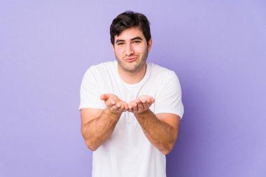 Mor arka planda izole edilmiş genç adam dudakları katlıyor ve hava öpücüğü vermek için avuç içleri tutuyor..