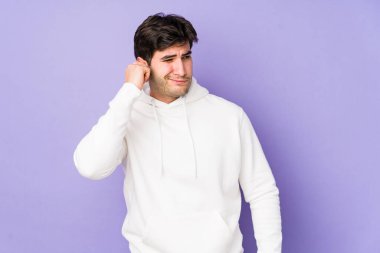 Mor arka planda izole edilmiş genç bir adam kulakları parmaklarıyla kapatıyor, gürültülü bir ortam yüzünden stresli ve çaresiz..