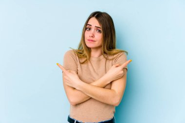 Mavi arka plan noktalarında izole edilmiş genç beyaz kadın iki seçenek arasında seçim yapmaya çalışıyor..