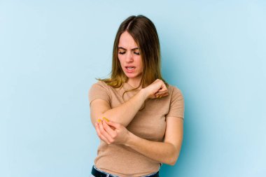 Beyaz bir kadın mavi arka planda izole edilmiş dirsek masajı yapıyor, kötü bir hareketin ardından acı çekiyor..