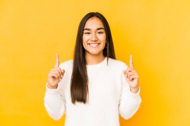 Sarı arka planda izole edilmiş genç bir kadın iki ön parmağı da boş bir alan gösteriyor..