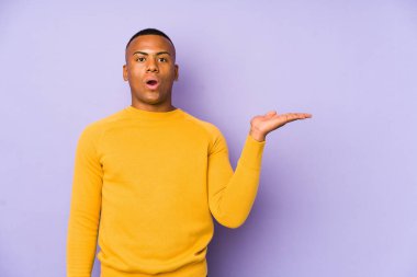 Mor arka planda izole edilmiş genç latin adam, avuç içi fotokopi alanını tutmaktan etkilenmiş..