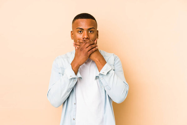 Young latin man isolated on beige background shocked covering mouth with hands.