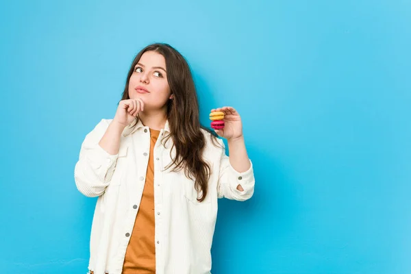 Jonge Bochtige Vrouw Houdt Macarons Kijken Zijwaarts Met Twijfelachtige Sceptische — Stockfoto