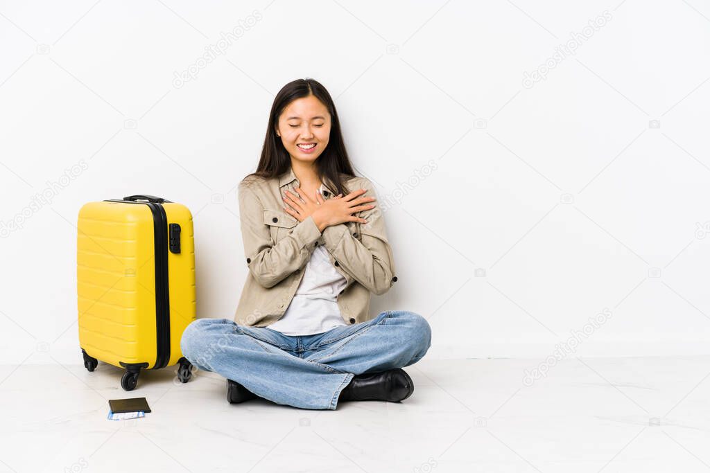 Young chinese traveler woman sitting holding a boarding passes laughing keeping hands on heart, concept of happiness.