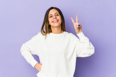 Mor arka planda izole edilmiş genç bir kadın iki numarayı parmaklarıyla gösteriyor..