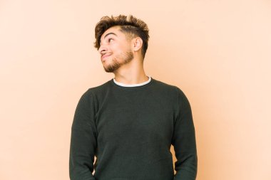 Genç Arap adam bej bir arka planda izole edilmiş hedeflerine ve amaçlarına ulaşma hayali kuruyor.