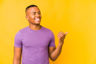 Genç latin adam sarı arka planda izole edilmiş, başparmak uzakta, gülüyor ve kaygısız..