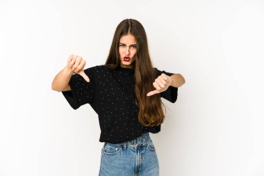 Beyaz arka planda izole edilmiş genç beyaz kadın baş parmağını aşağı gösteriyor ve hoşlanmadığını ifade ediyor..