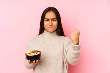 Makarna tutan genç Asyalı kadın kameraya yumruk gösteriyor, agresif yüz ifadesi var..