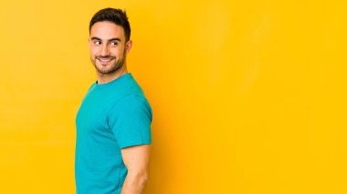 Sarı fırında izole edilmiş genç beyaz adam gülümseyen, neşeli ve keyifli bir tarafa bakıyor..