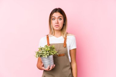 Pembe arka planda beyaz bir bahçıvan kadın omuzlarını silker ve gözleri açık bakar..
