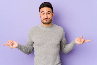 Mor arka planda izole edilmiş genç beyaz adam sorgulama sırasında omuz silkiyor ve şüphe duyuyor..