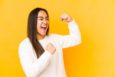 Sarı arka planda izole edilmiş genç bir kadın zaferden sonra yumruk kaldırıyor, kazanan konsept..