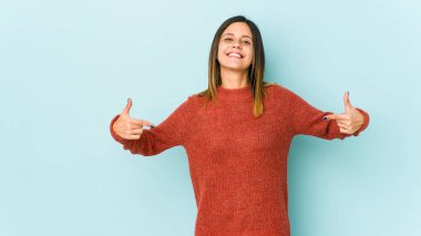 Mavi arka planda izole edilmiş genç bir kadın parmakları aşağıda, olumlu hisler içinde..